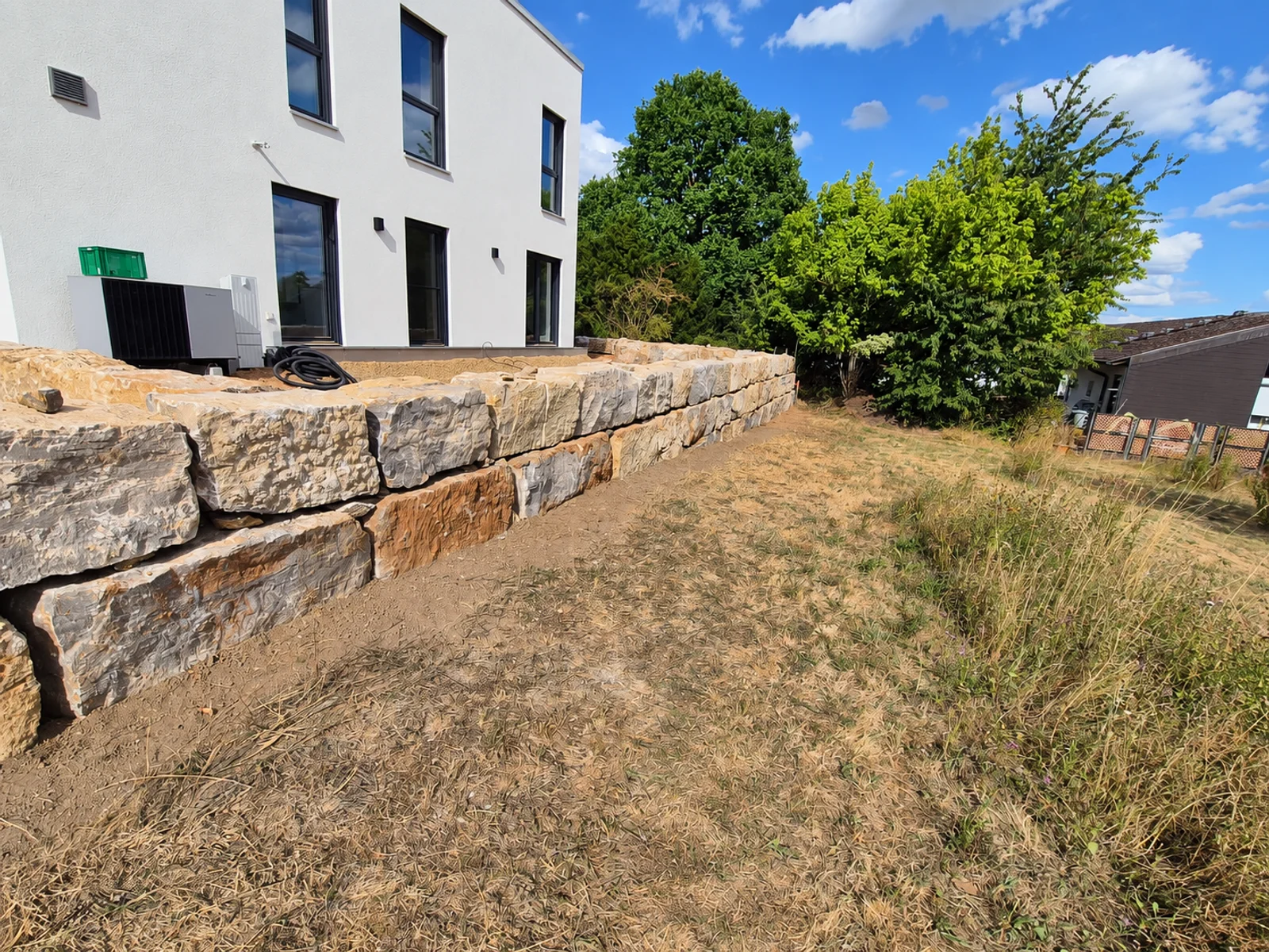Zweireihige Natursteinmauer entlang einer Außenanlage am Wohnhaus